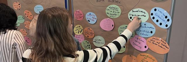 Eine Person pinnt bei einem Workshop ein Postit an eine Posterwand